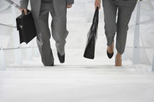 Lowsection of two businesspeople walking up stairs with bags in
