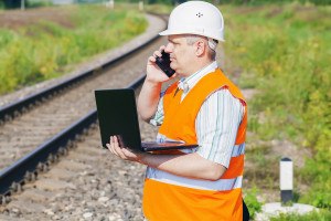 Railway Engineer with smartphone and laptop near railway