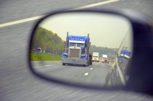 Large truck traveling down a highway as seen through a side view mirror