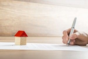 Closeup of new homeowner signing a contract of house sale or mortgage papers with a wooden toy house on the document. Suitable for real estate concept.